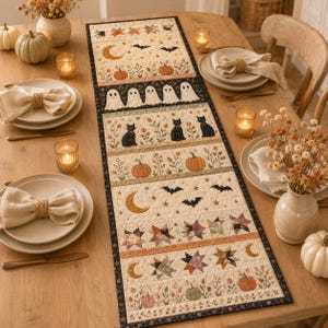 May include: A rectangular quilted table runner featuring a repeating pattern of Halloween motifs including ghosts, black cats, pumpkins, bats, stars, and crescent moons in muted earth tones, bordered by a thin black fabric trim with a floral design.