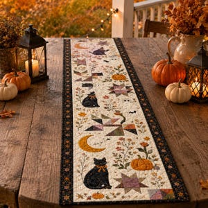May include: A rectangular quilted table runner featuring a cream-colored fabric base with a repeating pattern of black cats, orange pumpkins, yellow crescent moons, and geometric star shapes, bordered by a dark fabric with small floral motifs.