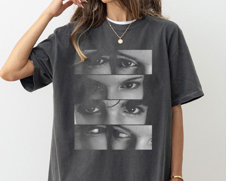 Puede incluir: Una camiseta gris antracita con un estampado gr&aacute;fico en blanco y negro de cuatro pares de ojos. Los ojos est&aacute;n dispuestos en una pila vertical.