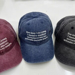 May include: Three baseball caps in burgundy, navy blue, and charcoal grey. Each cap has the embroidered text: "Ever since I was young I wanted to transform unstructured data into actionable business insights."