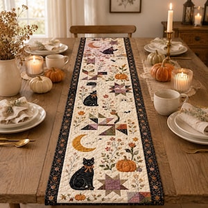 May include: A rectangular fabric table runner featuring a cream-colored center panel with a repeating pattern of black cats, orange crescent moons, pumpkins, stars, and floral motifs, bordered by a dark fabric with small orange and white accents.