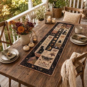 May include: A rectangular table runner featuring a patchwork design with celestial motifs, including moons, stars, a black cat, and a moth, set against a dark border. The fabric displays a cream background with floral and geometric patterns.