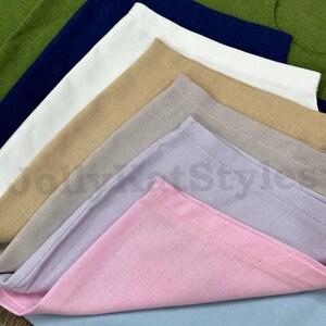 May include: A stack of folded cloth napkins in various colors, including green, navy blue, white, tan, gray, lavender, pink, and light blue. The napkins are made of a textured fabric and are neatly arranged, showcasing their different hues.