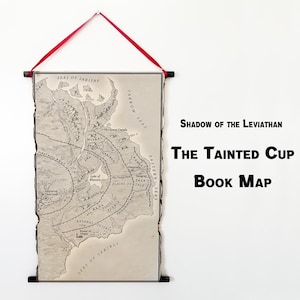 May include: A framed map print with a red ribbon for hanging. The map is in grayscale, with detailed geographical features and text. The text on the map reads "Shadow of the Leviathan" and "The Tainted Cup Book Map".