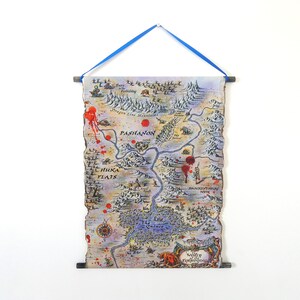 Puede incluir: Una impresión de mapa de fantasía con una cinta azul para colgar. El mapa presenta una ilustración detallada de un paisaje ficticio con montañas, ríos y asentamientos. El mapa está en tonos de azul, marrón y beige, con acentos rojos.