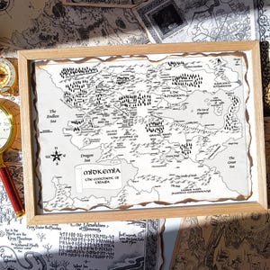 以下が含まれることがあります： 木製のフレームに入った、ミッドケミア大陸の地図。地図は白黒で、詳細な地理的特徴が描かれています。コンパスと赤い柄の虫眼鏡が地図の隣にあります。