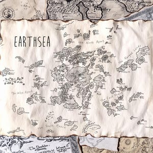 Può includere: Una mappa dettagliata di Earthsea, con intricate illustrazioni di isole e caratteristiche geografiche. La mappa è stampata su carta invecchiata con il titolo "EARTHSEA" in alto. Altre mappe sono visibili sullo sfondo.