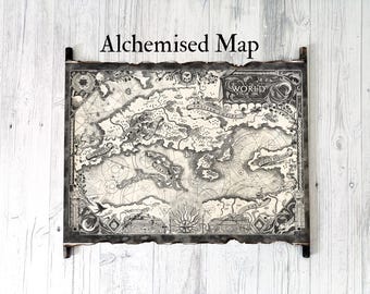 Könnte beinhalten: Eine detaillierte Schwarz-Weiß-Karte mit dem Titel "Alchemised Map" mit komplizierten Illustrationen von Landmassen, Ozeanen und Himmelselementen. Die Karte ist mit dunklem Holz gerahmt und hat ein gealtertes Aussehen, montiert auf einem hellen Holzgrund.