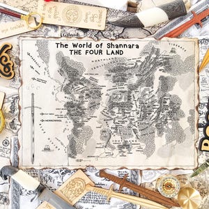 Puede incluir: Una composición de objetos de fantasía. Un mapa de "El Mundo de Shannara" está rodeado de espadas de madera, una brújula, una lupa y letreros de "Books". La escena evoca una sensación de aventura y lectura.