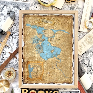 Puede incluir: Un mapa enmarcado de Temeria, con una representaci&oacute;n detallada de una tierra ficticia, con un gran lago azul y territorios circundantes. El mapa est&aacute; en un marco de madera, con la palabra "Temeria" en la parte superior. La palabra "BOOKS" est&aacute; en la parte inferior.