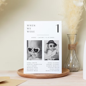 Puede incluir: Una tarjeta de mesa de boda en blanco y negro con el texto "WHEN WE WERE" y el n&uacute;mero "1". La tarjeta presenta dos fotos de beb&eacute;s con gafas de sol y enumera nombres debajo. La tarjeta est&aacute; sobre una bandeja de madera.