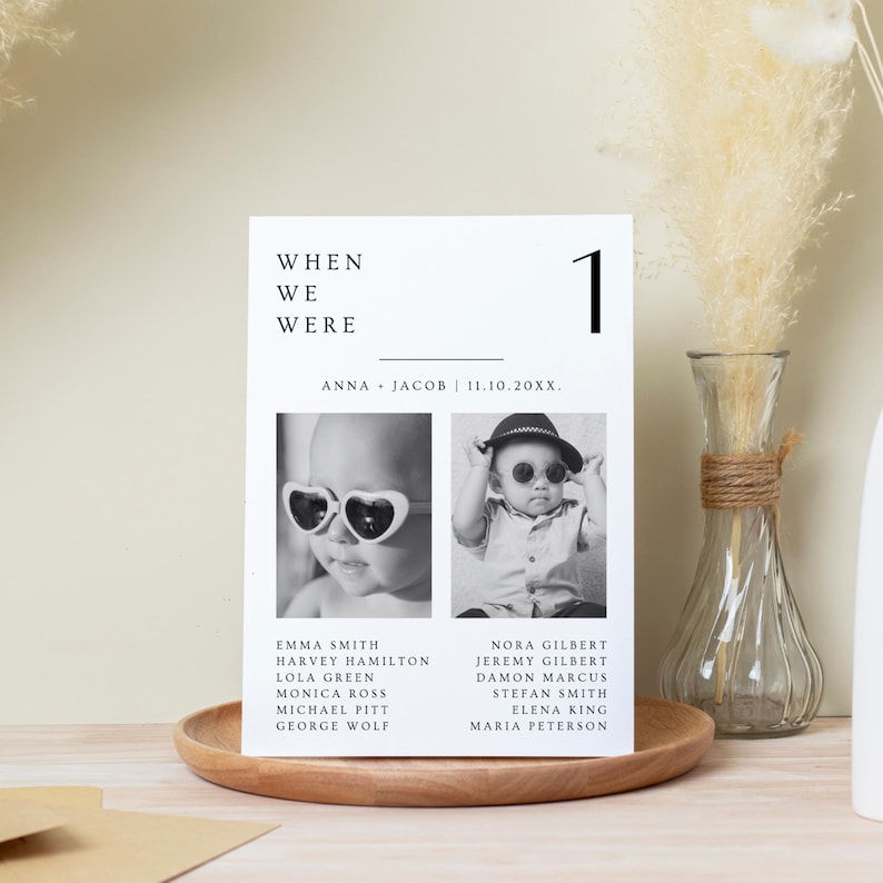 Puede incluir: Una tarjeta de mesa de boda en blanco y negro con el texto "WHEN WE WERE" y el n&uacute;mero "1". La tarjeta presenta dos fotos de beb&eacute;s con gafas de sol y enumera nombres debajo. La tarjeta est&aacute; sobre una bandeja de madera.