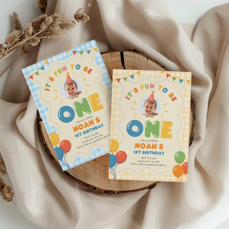 May include: Two birthday invitations with a photo of a child wearing a party hat. The invitations have the text "IT'S FUN TO BE ONE" and "NOAH'S 1ST BIRTHDAY" with colorful balloons and a gingham pattern.