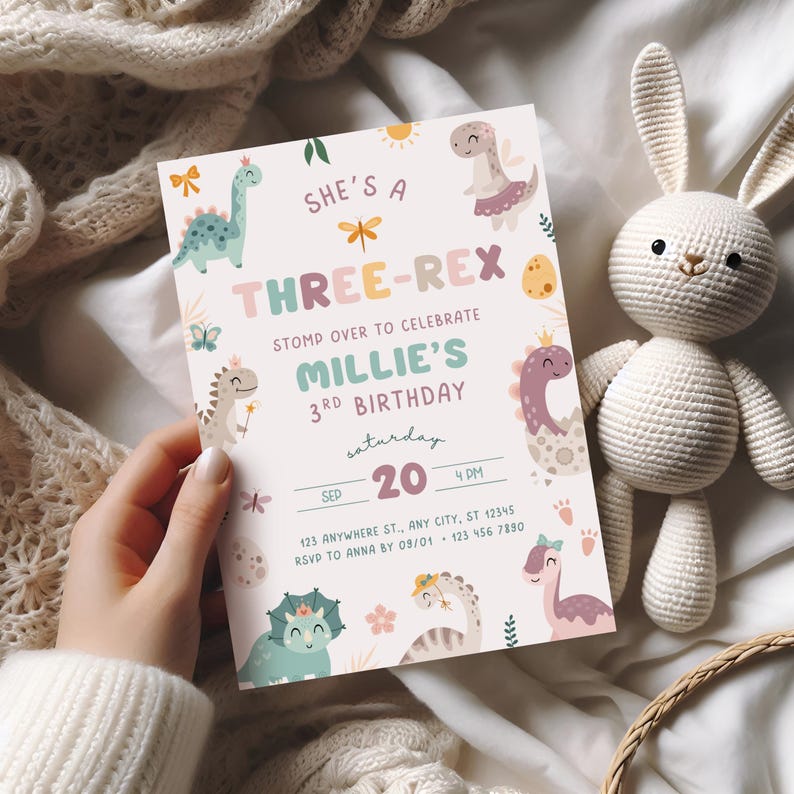 Pode incluir: Um convite em tons pastel com ilustra&ccedil;&otilde;es de dinossauros e o texto "SHE'S A THREE-REX" &eacute; segurado em uma m&atilde;o. O convite &eacute; para uma festa de terceiro anivers&aacute;rio, com o nome "Millie" e a data "20 de setembro". Um coelho de croch&ecirc; branco est&aacute; no fundo.