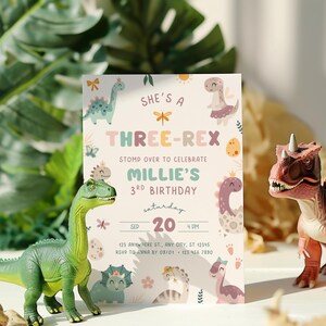 Pode incluir: Um convite de anivers&aacute;rio com tema de dinossauro. O convite diz "She's a Three-Rex" e inclui o texto "Stomp over to celebrate Millie's 3rd Birthday". Dois dinossauros de brinquedo est&atilde;o em primeiro plano.