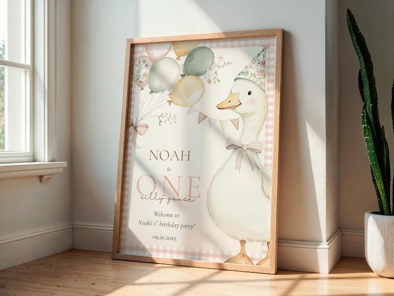 May include: A framed watercolor print featuring a goose wearing a party hat and bow tie, with balloons and the text "Noah is ONE silly goose." The print has a light wood frame and a pink and white checkered border.