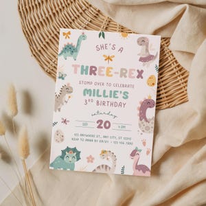 Pode incluir: Um convite de anivers&aacute;rio em tons pastel com ilustra&ccedil;&otilde;es de dinossauros. O texto diz "She's a Three-Rex" e anuncia o 3&ordm; anivers&aacute;rio de Millie em 20 de setembro &agrave;s 16h. O design inclui v&aacute;rios personagens de dinossauros e detalhes florais.