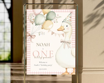 Puede incluir: Un letrero de fiesta con un ganso de dibujos animados que lleva un gorro de fiesta floral y una pajarita, sosteniendo globos. El letrero dice "Noah is One silly goose" con un mensaje de bienvenida para la primera fiesta de cumpleaños de Noah. El fondo tiene un patrón de cuadros rosas.