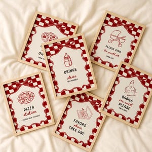 May include: Six framed signs with a red and white chequered border and a red ribbon design. Each sign features a different illustration and text, including a pizza, baby bottle, and a pram. The signs are for a party or event.