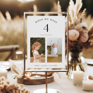 May include: A framed table number with the text "WHEN WE WERE 4". The frame holds two photos of a young child. The bottom of the frame reads "ANNA + JACOB | 11.10.20XX.". The frame is displayed on a gold stand.