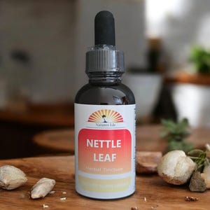 Könnte beinhalten: Eine dunkle Glasflasche mit Nesselblatt-Kräutertinktur und einer Pipette. Das Etikett zeigt den Text "Nettle Leaf" in einem roten und orangen Farbverlauf mit "Herbal Tincture" darunter. Die Flasche steht auf einer Holzoberfläche.