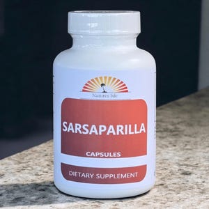 May include: A white plastic bottle of Sarsaparilla capsules. The label is red and white with the text "Sarsaparilla Capsules Dietary Supplement" and the brand name "Natures Isle". The bottle has a white cap.