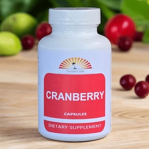 May include: A white bottle of cranberry capsules with a red label. The label reads "CRANBERRY CAPSULES DIETARY SUPPLEMENT" with the "Natures Isle" logo above. Red cranberries and green fruit are in the background.