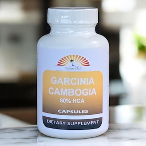 Puede incluir: Una botella blanca de cápsulas de Garcinia Cambogia. La etiqueta presenta el texto "Garcinia Cambogia 60% HCA" y "Suplemento dietético". La botella tiene una tapa blanca y un logotipo de un sol sobre el océano.