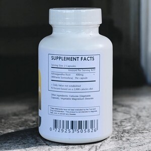 Op de afbeelding: Een witte supplementfles met een witte dop. Het etiket toont "SUPPLEMENT FACTS" en ingredi&euml;nteninformatie, waaronder "Ashwagandha Root" en "400mg". De fles bevat ook andere ingredi&euml;nten en een streepjescode.