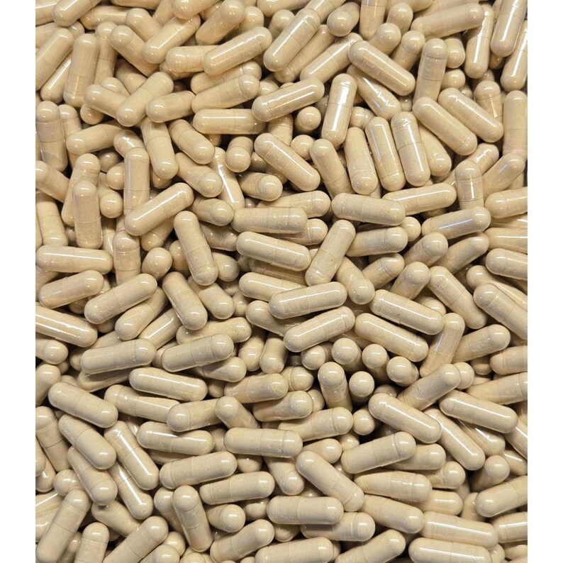 Op de afbeelding: Een close-up van talrijke beige capsules, dicht op elkaar gepakt. De capsules hebben een gladde, cilindrische vorm met afgeronde uiteinden. De belichting benadrukt de textuur- en kleurvariaties, waardoor een gevoel van diepte ontstaat. De afbeelding suggereert een gezondheids- of supplementproduct.