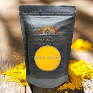 May include: A dark gray pouch of organic turmeric powder with the text "ORGANIC TURMERIC" in a yellow circle. The pouch has a decorative pattern and the logo "NATURE'S ISLE". Yellow turmeric powder is scattered on a wooden surface.