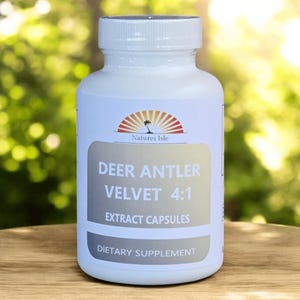 以下が含まれることがあります： 白いキャップが付いた白いサプリメントボトル。ラベルには「Deer Antler Velvet 4:1 Extract Capsules」と「Dietary Supplement」と記載されています。「Natures Isle」のブランド名も表示されています。背景はぼやけた緑色です。