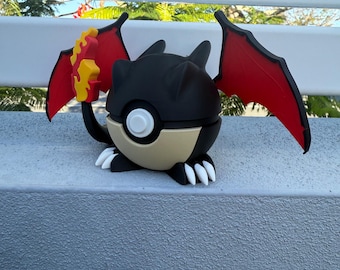 Könnte beinhalten: Eine schwarze und rote Pokémon-Figur mit einem Pokeball-Design. Die Figur hat Flügel und einen Schwanz.