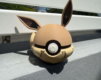 May include: A brown and tan 3D printed Pokémon figure of Eevee in its Poké Ball form. The figure has large ears and a white Poké Ball design on its chest.