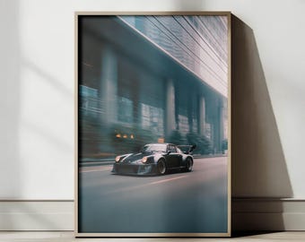 Può includere: Stampa incorniciata di un'auto sportiva nera che sfreccia su una strada cittadina. L'auto, con una grande ala posteriore, è ambientata su uno sfondo sfocato di edifici e cielo blu. La stampa è in una cornice di legno.