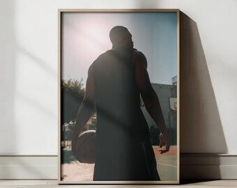 Può includere: Stampa incorniciata di un giocatore di basket di spalle, con un pallone. Il sole splende sullo sfondo. L'immagine è ambientata su un campo da basket, con un canestro visibile.