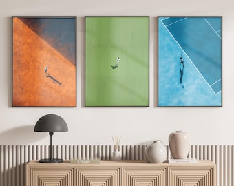 Può includere: Un set di tre stampe artistiche da parete verticali incorniciate che mostrano viste aeree di campi da tennis in arancione, verde e blu. Ogni stampa mostra un singolo giocatore sulla superficie del campo con ombre visibili, in cornici nere sottili.