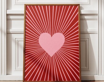 Può includere: Una stampa artistica incorniciata con un grande cuore rosa al centro, che irradia con linee rosa su uno sfondo rosso. L'opera d'arte è racchiusa in una cornice di legno marrone, creando un contrasto visivo sorprendente.