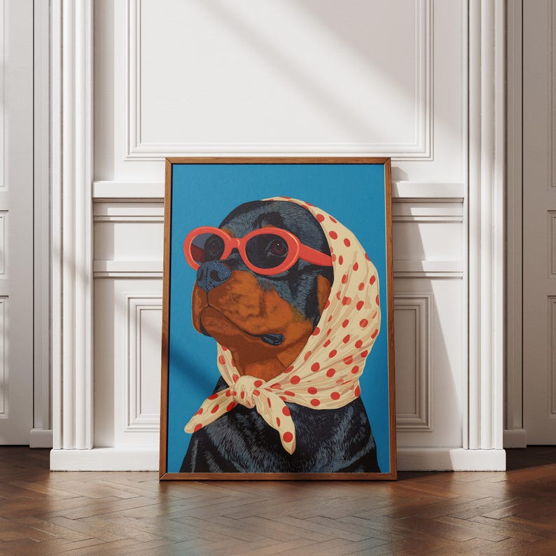 Puede incluir: Una impresi&oacute;n art&iacute;stica enmarcada que presenta a un perro Rottweiler con gafas de sol rojas y un pa&ntilde;uelo crema con lunares rojos. El perro est&aacute; sobre un fondo azul brillante. La obra de arte est&aacute; en un marco de madera.