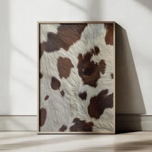 Może przedstawiać: Oprawiony wydruk przedstawiający zbliżenie wzoru skóry krowy. Skóra prezentuje mieszankę białych i brązowych plam, z brązowymi obszarami o nieregularnych kształtach. Rama jest w kolorze jasnego drewna, a wydruk jest na białej ścianie.