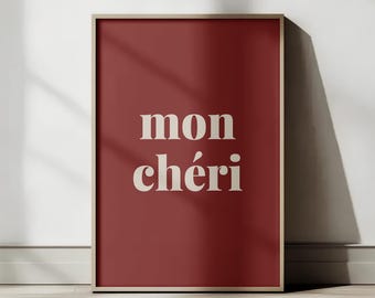 Può includere: Una stampa artistica incorniciata con sfondo rosso scuro. Le parole "mon chéri" sono visualizzate in un carattere serif color crema. La cornice è di colore marrone chiaro e la stampa è appoggiata a una parete bianca.