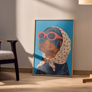 Puede incluir: Una impresi&oacute;n art&iacute;stica enmarcada que presenta a un perro Rottweiler con gafas de sol rojas y un pa&ntilde;uelo blanco con lunares rojos. El perro est&aacute; sobre un fondo azul. La obra de arte est&aacute; en un marco de madera.