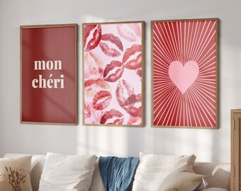 Può includere: Tre stampe artistiche incorniciate con un tema romantico. La stampa a sinistra è uno sfondo rosso pieno con le parole "mon chéri" in bianco. La stampa centrale presenta un motivo di baci di rossetto rosso su sfondo rosa. La stampa a destra ha un cuore rosa con raggi rossi.