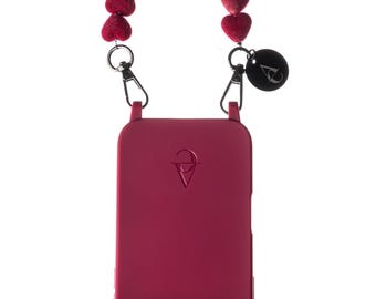 Può includere: Una custodia per smartphone color magenta con un cinturino da polso composto da perline a forma di cuore, fissato tramite chiusure in metallo argentato. La custodia presenta un logo in rilievo vicino alla parte superiore e un'apertura argentata per il modulo fotocamera. Un piccolo ciondolo nero rotondo con un logo bianco è appeso a una delle chiusure.