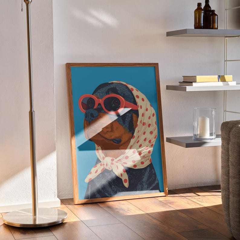 Puede incluir: Impresi&oacute;n art&iacute;stica enmarcada que presenta un perro Rottweiler con gafas de sol rojas y un pa&ntilde;uelo crema con lunares rojos. El perro est&aacute; sobre un fondo azul. La obra de arte est&aacute; en un marco de madera.