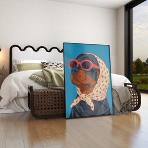 Puede incluir: Impresi&oacute;n art&iacute;stica enmarcada que presenta un perro Rottweiler con gafas de sol rojas y un pa&ntilde;uelo de lunares. La obra de arte se exhibe en un dormitorio, apoyada contra una cama, sobre un fondo azul.