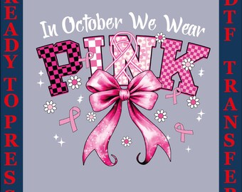 Op de afbeelding: Een roze en grijs DTF-transferontwerp met de tekst "In October We Wear PINK". Het woord PINK is in een mix van geruite en bloemmotieven. Een grote roze strik en roze linten zijn afgebeeld.