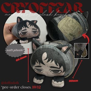 Könnte beinhalten: Grauer Plüsch-Schlüsselanhänger mit einer Figur, die eine katzenartige Kapuze trägt. Der Schlüsselanhänger hat schwarze Akzente und rosa Innenohren. Der Plüsch misst 9 cm lang und 6,05 cm hoch. Der Text "soft plush!" ist sichtbar.