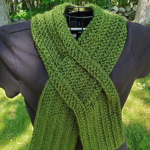 May include: A green crocheted scarf with a criss-cross pattern. The scarf is displayed on a black shirt.