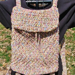 May include: A multi-colored crocheted bag with a drawstring closure and a long strap. The bag is made with a variety of shades of pink, blue, green, and beige yarn.